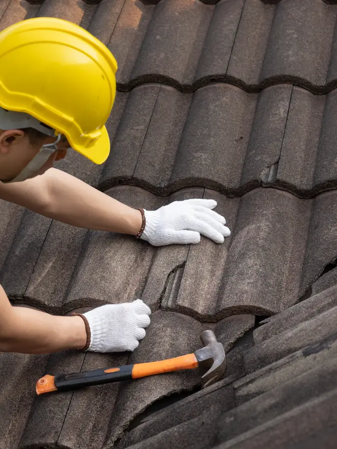 Roofer fixing a concrete roof tile with a hammer