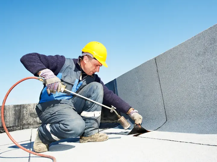Roofer sealing a flat roof membrane against an upstand