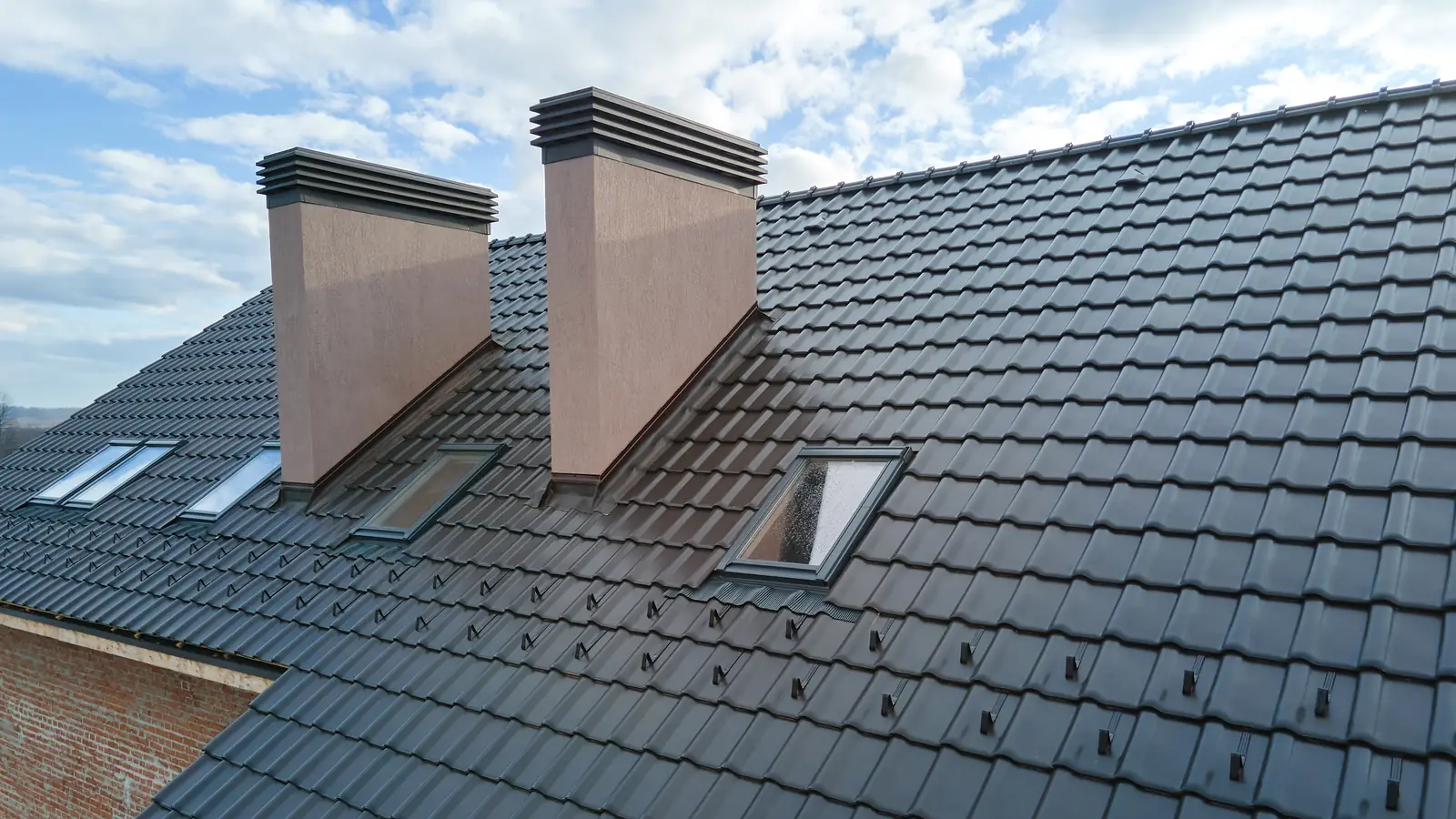 Grey tiled roof with chimneys and roof windows