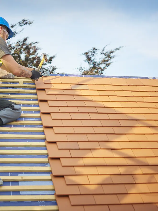 Roofer laying new clay tiles on a re-roof
