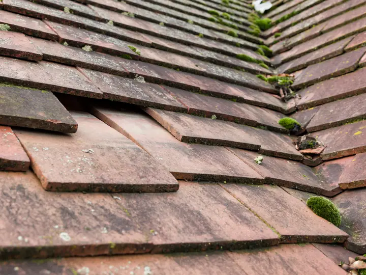 Worn and slipped tiles beside a chimney on a pitched roof